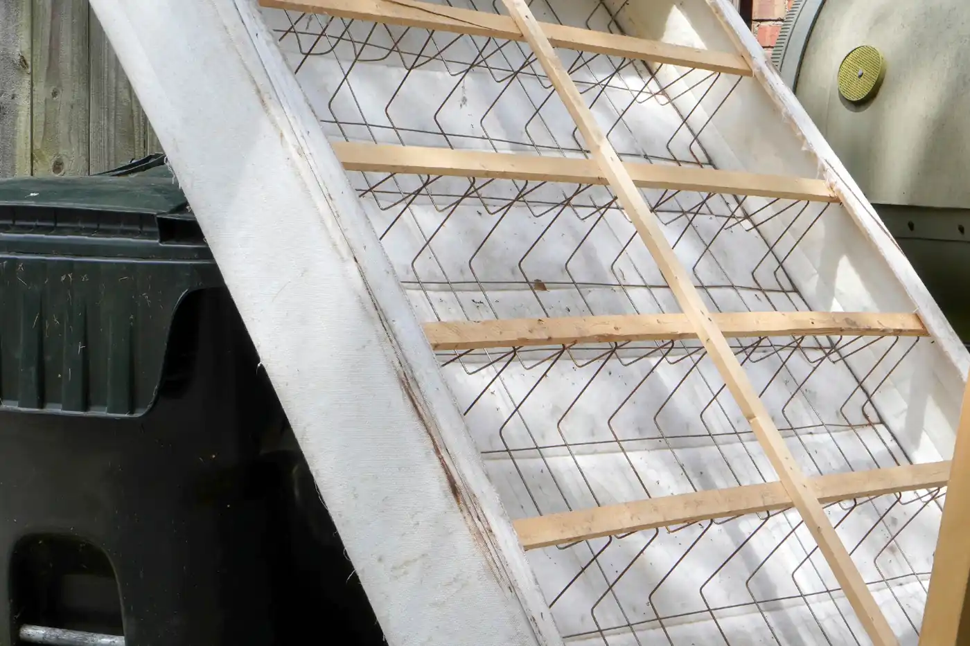 Box spring leaning against a curbside trash cart
